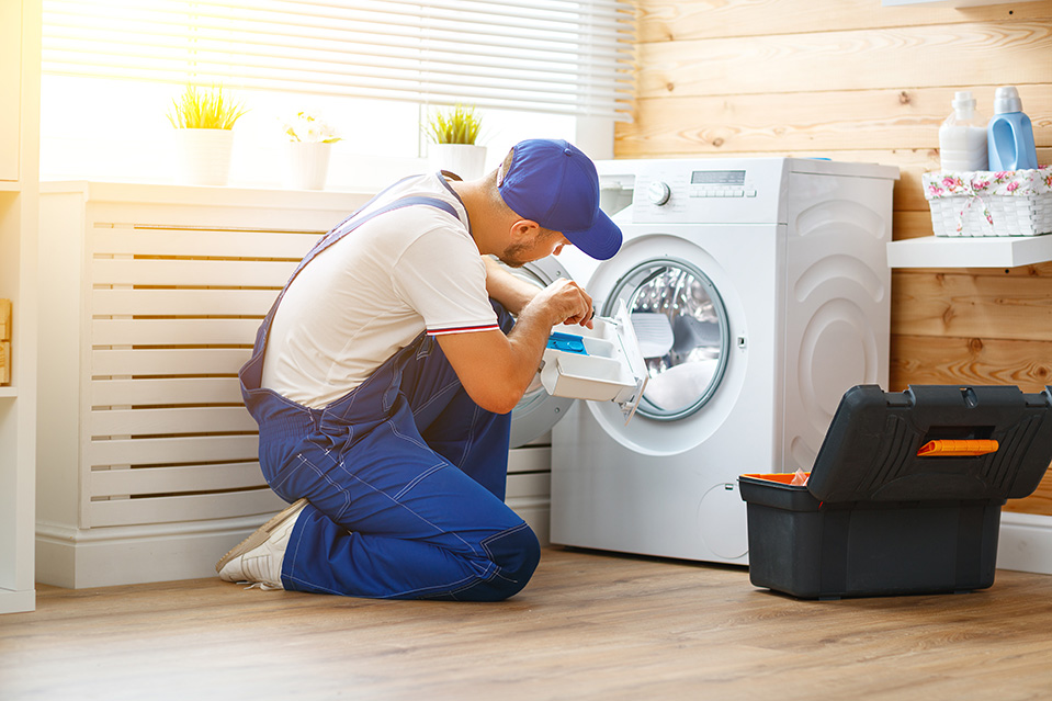 working man plumber repairs washing machine in laundry working man plumber repairs a washing machine in laundry